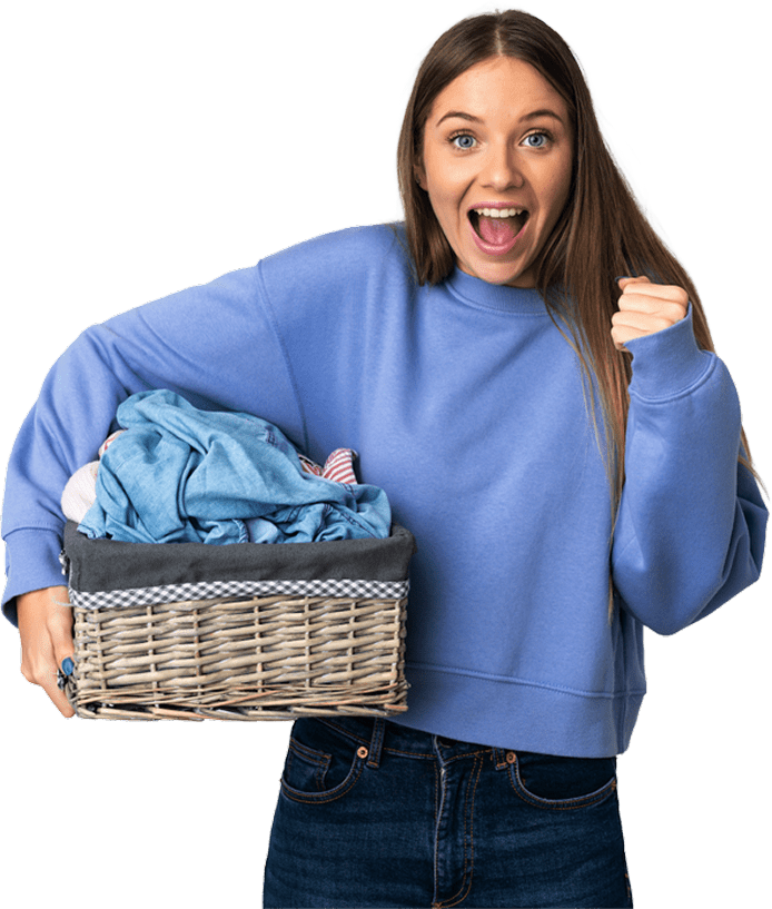 Young woman holding a laundry basket filled with clothes, smiling and raising her fist in a celebratory gesture.