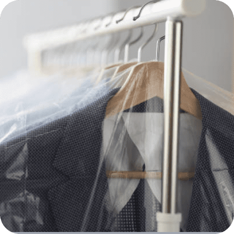 A row of suit jackets on hangers, covered in clear plastic garment bags, hangs on a white clothing rack.