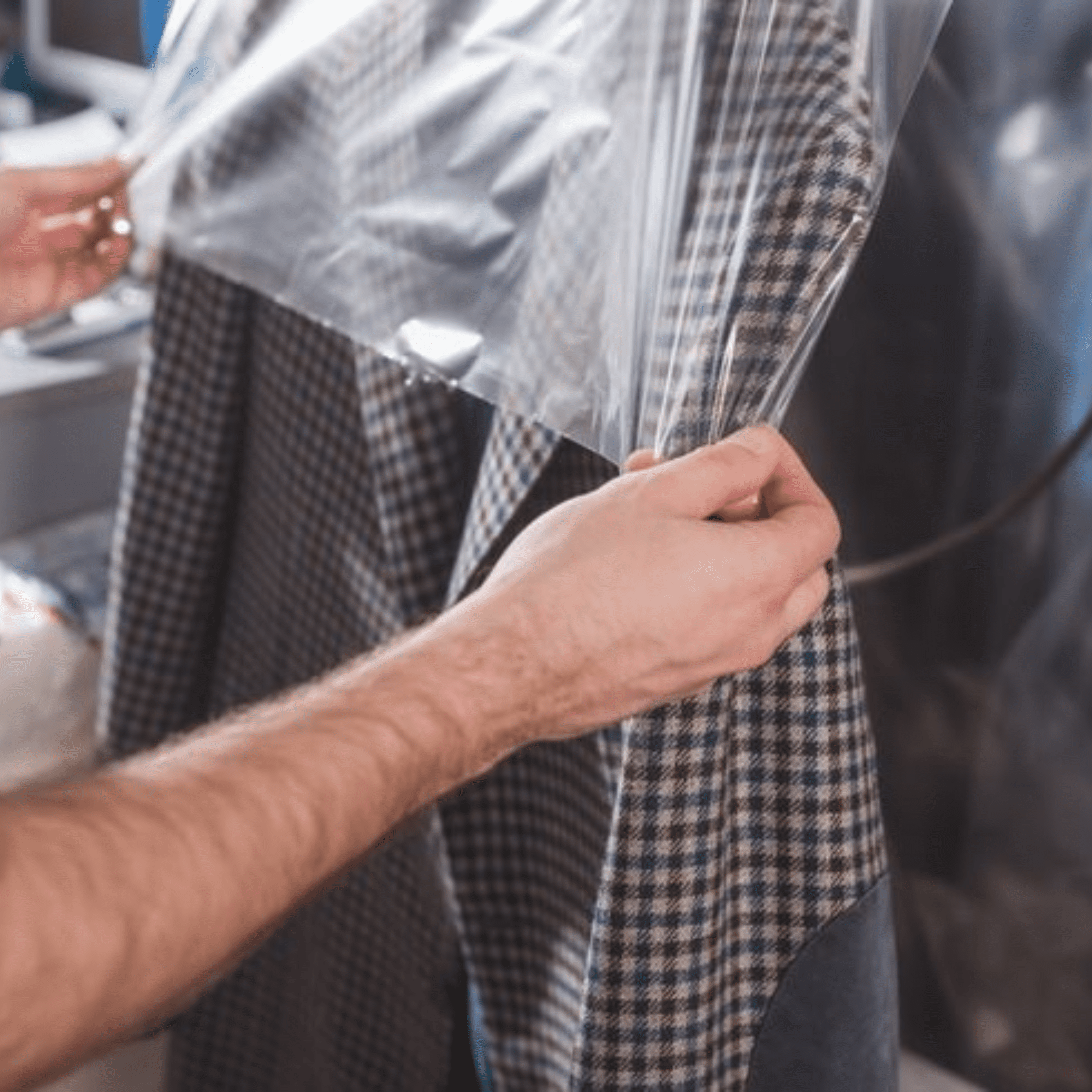 A person covers a plaid jacket with a clear plastic garment bag, likely for storage or dry cleaning purposes.