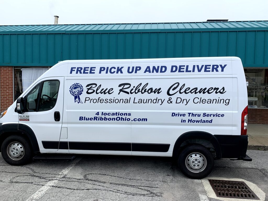 White Blue Ribbon Cleaners van with blue text advertising free pick up and delivery, professional laundry and dry cleaning, and four Ohio locations. Parked in front of a teal building.