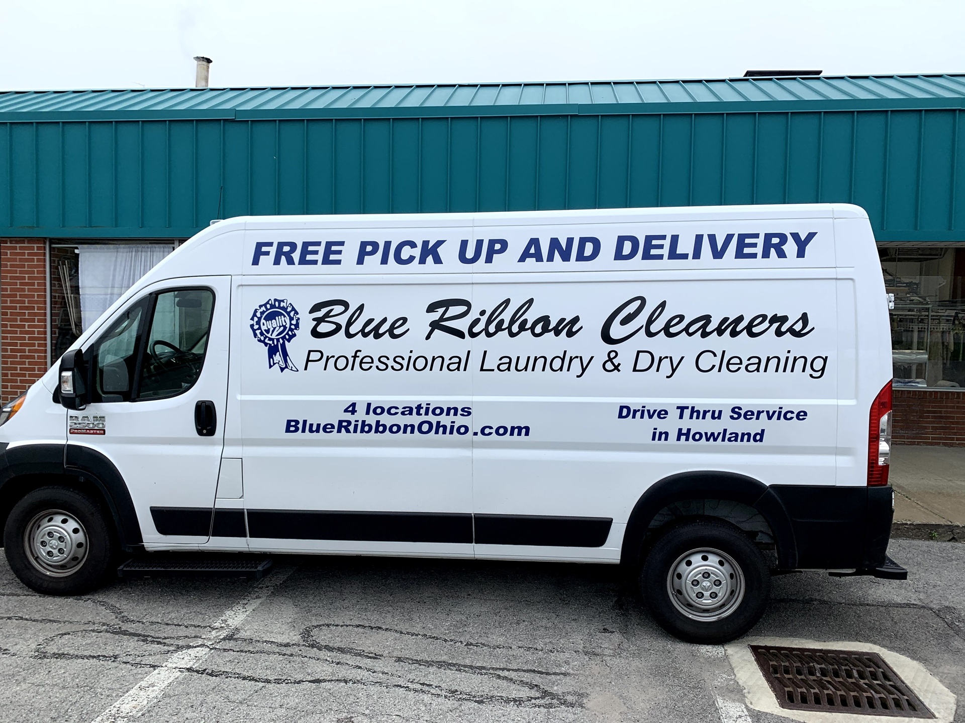 White Blue Ribbon Cleaners van with blue text advertising free pick up and delivery, professional laundry and dry cleaning, and four Ohio locations. Parked in front of a teal building.