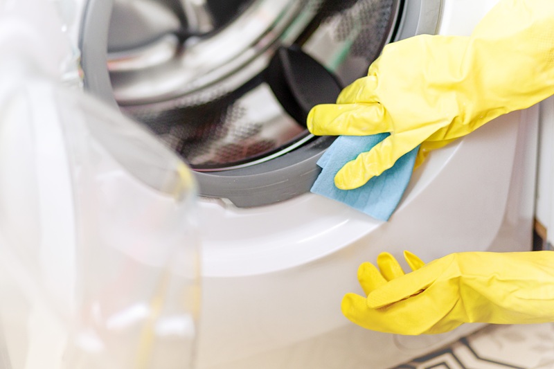 Person wearing yellow rubber gloves cleaning the door seal of a washing machine with a blue cloth.